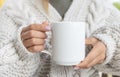 White ceramic mug mockup. Woman in Sweater Holding a Warm Cup of Coffee. Copy space for your print