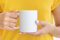White ceramic mug mockup. Woman wears yellow t-shirt Holding a Warm Cup of Coffee. Copy space for your logo Royalty Free Stock Photo