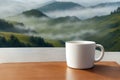 White ceramic mug on a wooden table with a blurred background view of misty hills