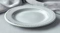 A white ceramic plate with beaded edge detailing lies on a textured gray fabric surface. Royalty Free Stock Photo