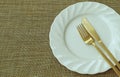 White Ceramic Plate and Brass Cutlery on Beige Luncheon Mat with Free Space for Text and Design Royalty Free Stock Photo