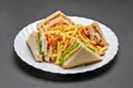 White ceramic plate with French fries, four sandwiches with cheese, lettuce, tomato and ham