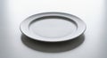 A white ceramic plate placed on a smooth, light gray surface. The plate has a simple, round form Royalty Free Stock Photo
