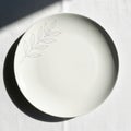A white ceramic plate with a simple black leaf design is centered on a white Royalty Free Stock Photo
