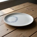 White ceramic plate on a wooden table, featuring a blue circular pattern of abstract loops and Royalty Free Stock Photo