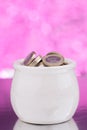 White ceramic pot with coins on pink background