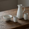 White ceramic tableware includes a pitcher, two bowls, and two cups with a simple, Royalty Free Stock Photo