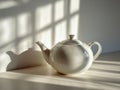 White ceramic teapot casting soft shadows on a sunlit surface with window patterns creating a calm and minimalist atmosphere in a Royalty Free Stock Photo
