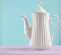 White ceramic teapot on a pastel purple wooden table isolated on a blue background. Copy space. Royalty Free Stock Photo