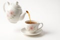 White ceramic teapot side view mid pour with a smooth tea stream entering the cup on white Royalty Free Stock Photo