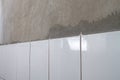 White ceramic tiles laid on a concrete gray wall in the bathroom, new tiles, the process of laying tiles on the wall Royalty Free Stock Photo