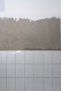 White ceramic tiles laid on a concrete gray wall in the bathroom, new tiles, the process of laying tiles on the wall Royalty Free Stock Photo