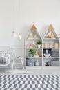 White chair between bed and shelves in kid`s bedroom interior wi