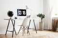 White chair at desk with black globe and desktop computer in home office interior with plant. Real photo Royalty Free Stock Photo