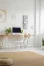 White chair at desk with computer desktop in home office interior with pouf on carpet. Real photo Royalty Free Stock Photo