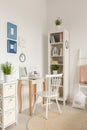 White chair at dressing table next to cabinet with plant in bedroom interior with posters. Real photo Royalty Free Stock Photo