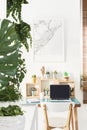 White chair standing by the simple wooden desk with cactuses, coffee cup, notebook and laptop in bright home office interior with Royalty Free Stock Photo