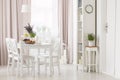 White chairs at dining table with plants in modern flat interior with pink drapes and window. Real photo Royalty Free Stock Photo