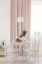 White chairs at table with flowers under lamp in dining room interior with pink drapes. Real photo Royalty Free Stock Photo