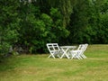 White chairs and table on lawn of garden in landscape format. Royalty Free Stock Photo