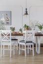 White chairs at wooden table in cottage dining room interior with flowers and poster. Real photo Royalty Free Stock Photo