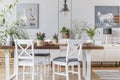 White chairs at wooden table with flowers in eclectic dining room interior with posters. Real photo Royalty Free Stock Photo