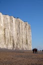 White chalk cliff face with pebble beach and people walking on t