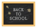 White chalk inscription Back to school and yellow autumn foliage on a blackboard in a wooden frame