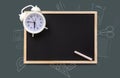 White chalk and a round white alarm clock with hands and dial, on a black empty blackboard. Outlines of school supplies, drawn in Royalty Free Stock Photo