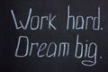 White chalk writing on a dark board `Work hard. Dream big.`