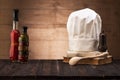 White chef`s hat and old cookbook on the kitchen table, wooden spoon and spices. Royalty Free Stock Photo