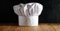 White chef`s hat and wooden table background with dark wall.