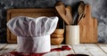 White chef`s hat and wooden table background with kitchen utensils