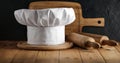 White chef`s hat and wooden table background with kitchen utensils