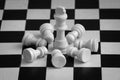 White chess pieces, king surrounded by lying pawns, on chessboard. Concept of leadership