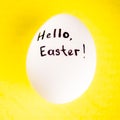 Closeup white chicken egg with black text - Hello, Eeaster on yellow table