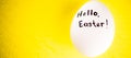 White chicken egg with black text - Hello, Eeaster on yellow table.