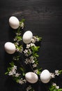 White chicken eggs lie in a flowering branch of cherry on a black wooden background. Conceptual easter layout