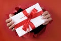 White Christmas or birthday surprise gift with ribbon being delivered through a red torn paper background