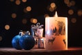 White Christmas candle, blue shiny balls and presents on a wooden table with garlands background