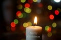 White Christmas candle light with text message and greeting - Merry Christmas. On colorful bokeh lights on dark background Royalty Free Stock Photo