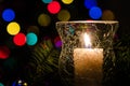 White Christmas Candle Surrounded by Christmas Lights and Evergreen Branches