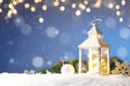 White Christmas lantern in snow, with yellow candle light, on blue background Royalty Free Stock Photo