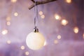 White Christmas Tree Ball Hanging on a Branch Golden Garland Glittering Lights in the background Festive Greeting Card Royalty Free Stock Photo