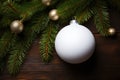 White Christmas tree toy ball decoration with a fluffy fir branch on wooden background.