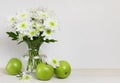 White chrysanthemum flowers bouquet in a glass vase and green apples at wooden table Royalty Free Stock Photo