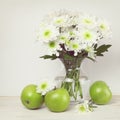 White chrysanthemum flowers bouquet in a glass vase and green apples at wooden table Royalty Free Stock Photo