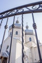 White church through iron fence. Ortodox cathedral on clear blue sky background. Religious architecture. Faith and pray concept.