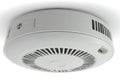 A white circular smoke detector mounted on a white ceiling featuring ventilation slots and a central sensor area Royalty Free Stock Photo