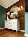 White classic chest of drawers with decor and a mirror in a frame on a background of a wooden wall with sconces